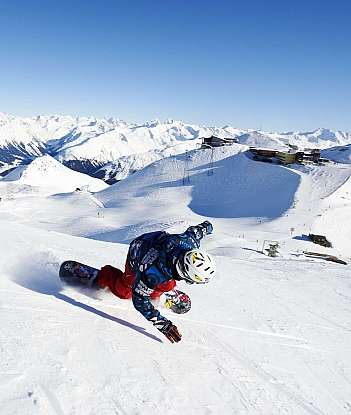 A snowboarder carving through fresh snow in a mountainous landscape.