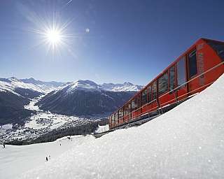 A red cable car overlooking snowy mountains and a valley.