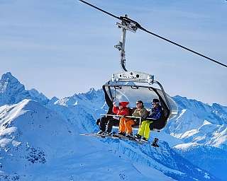 Four skiers riding a chairlift above snowy mountains.