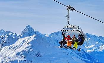 Four skiers riding a chairlift above snowy mountains.