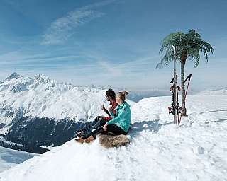 Zwei Personen genießen Getränke auf einem schneebedeckten Gipfel.