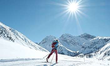 A skier traverses a snowy landscape under a bright sun.