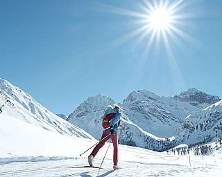 A skier traverses a snowy landscape under a bright sun.