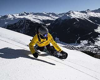 A snowboarder carving down a snowy slope with mountains in the background.