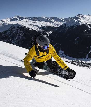 Ein Snowboarder fährt auf einem schneebedeckten Hang mit Bergen im Hintergrund.