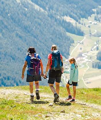 Three hikers walking on a mountain trail with scenic views.