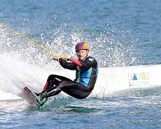 A wakeboarder performs a trick on water, splashing waves.