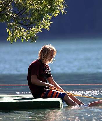 Ein Junge sitzt auf einem Floß und spielt mit einem Seil im Wasser.