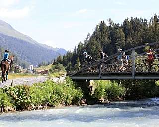 A horse rider and cyclists crossing a bridge in a scenic landscape.