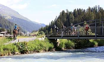 Un cavalier et des cyclistes traversent un pont en montagne.