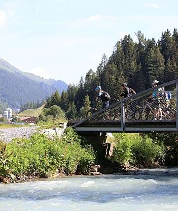 Un cavalier et des cyclistes traversent un pont en montagne.