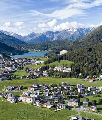 Village alpin entouré de montagnes et de forêts verdoyantes.