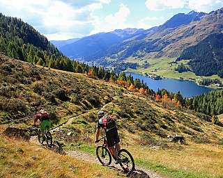 Deux cyclistes sur un sentier avec un lac et des montagnes en arrière-plan.