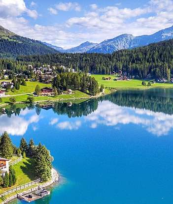 Vue panoramique d'un lac avec des maisons et des montagnes en arrière-plan.