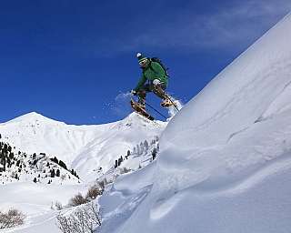 A person snowshoeing down a snowy slope against a blue sky.