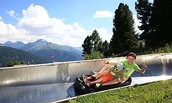 Zwei Kinder fahren fröhlich auf einer Rodelbahn in den Bergen.