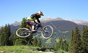 A mountain biker performs a jump against a scenic mountain backdrop.