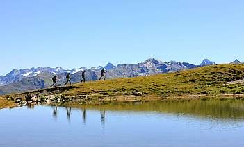 Hikers near a mountain lake Four hikers walking along a grassy hill by a tranquil lake.