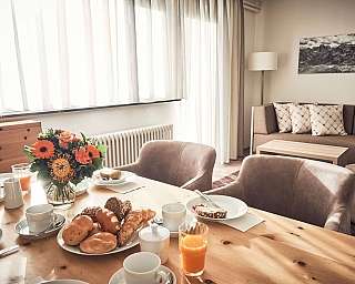 Ein Tisch mit Frühstück, Blumen und einem gemütlichen Wohnzimmer.