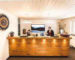 Two receptionists at a wooden desk in a modern office.