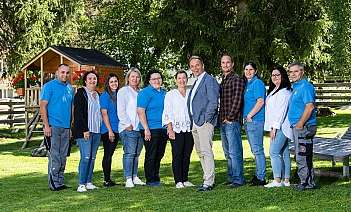 Vier Personen lächeln vor einer Holzhütte im Schnee.