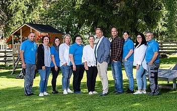 A family of four smiling in the snow near a wooden cabin.
