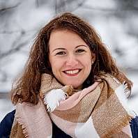 Woman smiling in snowy landscape A woman with curly hair wearing a scarf in a snowy setting.