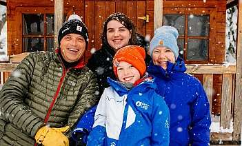 Quatre personnes souriantes devant un chalet enneigé.