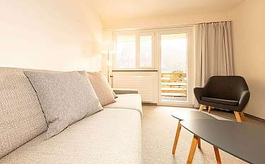 Gemütliches Wohnzimmer mit Sofa, Stuhl und Blick auf den Balkon.