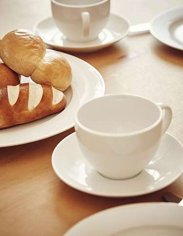 Ein Tisch mit Brötchen und weißen Kaffeetassen.