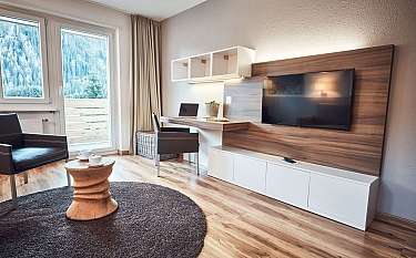 Helles Wohnzimmer mit Fernseher, Schreibtisch und Balkonblick.