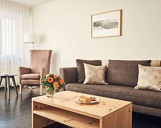 Ein helles Wohnzimmer mit Sofa, Blumen und einem Tisch.