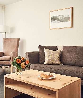 A comfortable living room with a sofa, flowers, and snacks.
