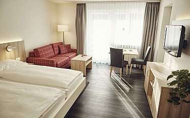 Gemütliches Hotelzimmer mit Bett, Sofa und Esstisch.