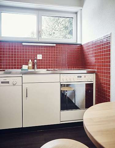 Küche mit Spüle, Geschirrspüler und roter Fliesenwand.