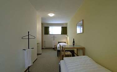 A minimalist hotel room with two beds and a table.
