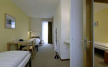 A spacious hotel room with two beds and a dining area.