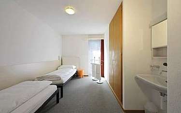 A minimalist bedroom with two beds and a washbasin.