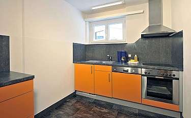 A contemporary kitchen featuring orange cabinets and stainless steel appliances.