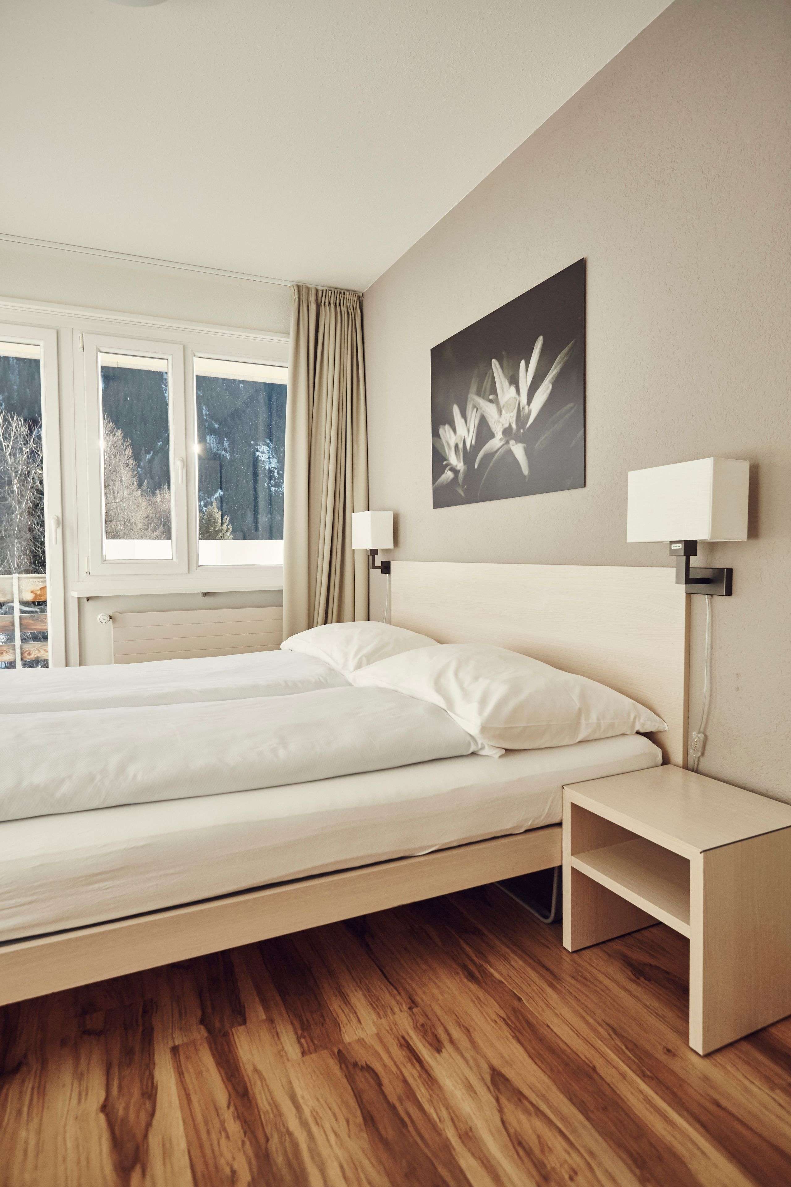 Helles, schlicht eingerichtetes Schlafzimmer mit Doppelbett, Nachttisch und Fenster.