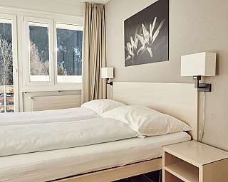 Helles Schlafzimmer mit Doppelbett, Nachttischlampe, Fenster und Wandbild über dem Bett.