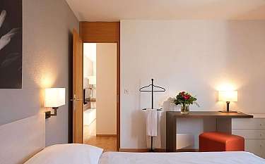 A well-lit hotel room with a bed, desk, and flowers.