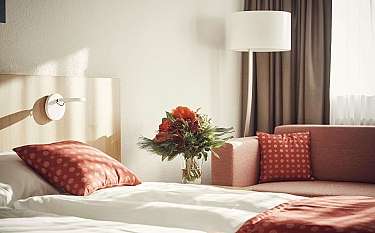 Gemütliches Hotelzimmer mit roten Kissen und Blumenarrangement.