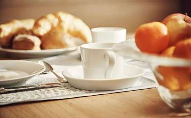 Ein gedeckter Tisch mit Croissants, Obst und einer Tasse.