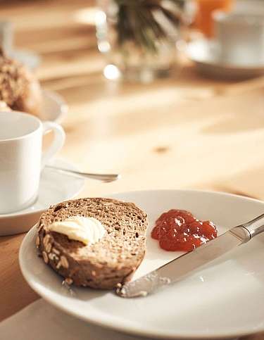 Ein Teller mit Brot, Butter und Marmelade neben einer Tasse.