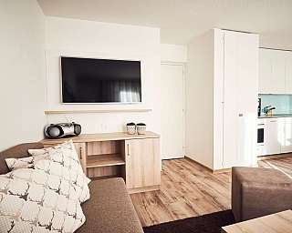 Gemütliches Wohnzimmer mit Fernseher und moderner Küchenecke.