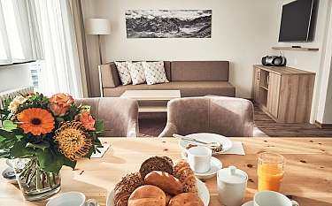 Ein Tisch mit Frühstück und Blumen in einem hellen Wohnzimmer.
