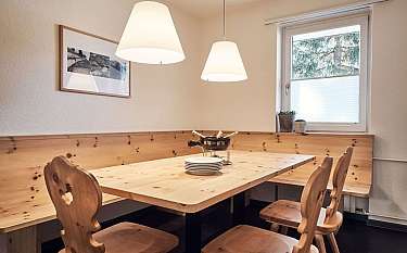 Gemütlicher Essbereich mit Holzbank und Tisch, beleuchtet von Pendelleuchten.