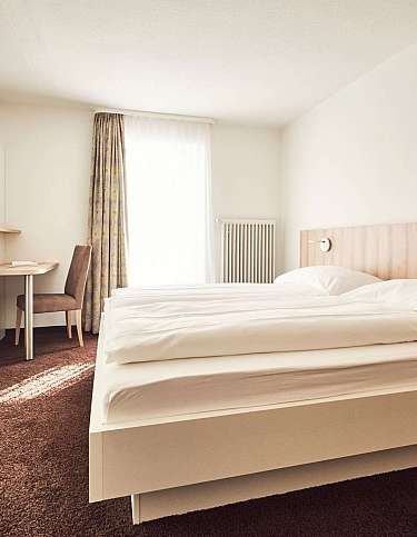 Modernes Hotelzimmer mit zwei Betten, Schreibtisch und Fernseher.