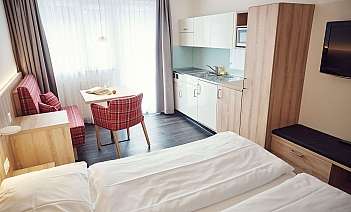 Helles Hotelzimmer mit Küchenzeile, Tisch und gemütlichen Sitzgelegenheiten.